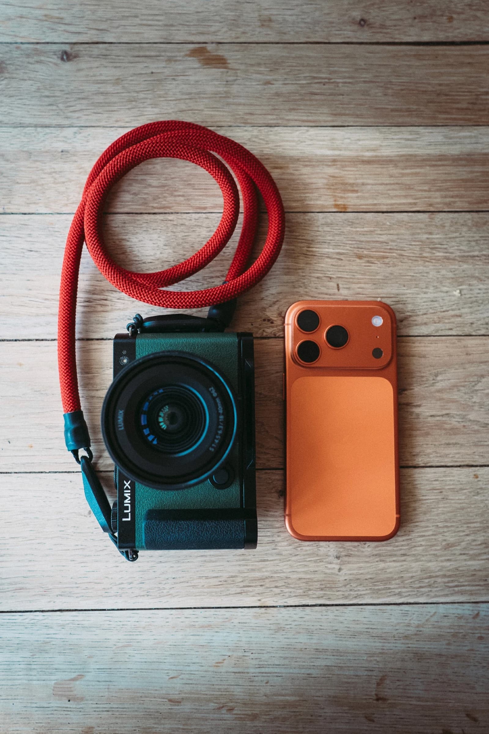 A Lumix camera and an orange iPhone on a wooden table, edited with the Made in Brighton pack
